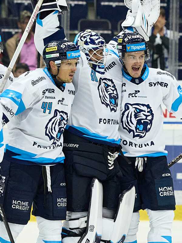 Eishockeyspieler mit Nummer 44 jubeln im Spiel, Torhüter mit Helm, drei Spieler in weißen Trikots mit blauen Akzenten.