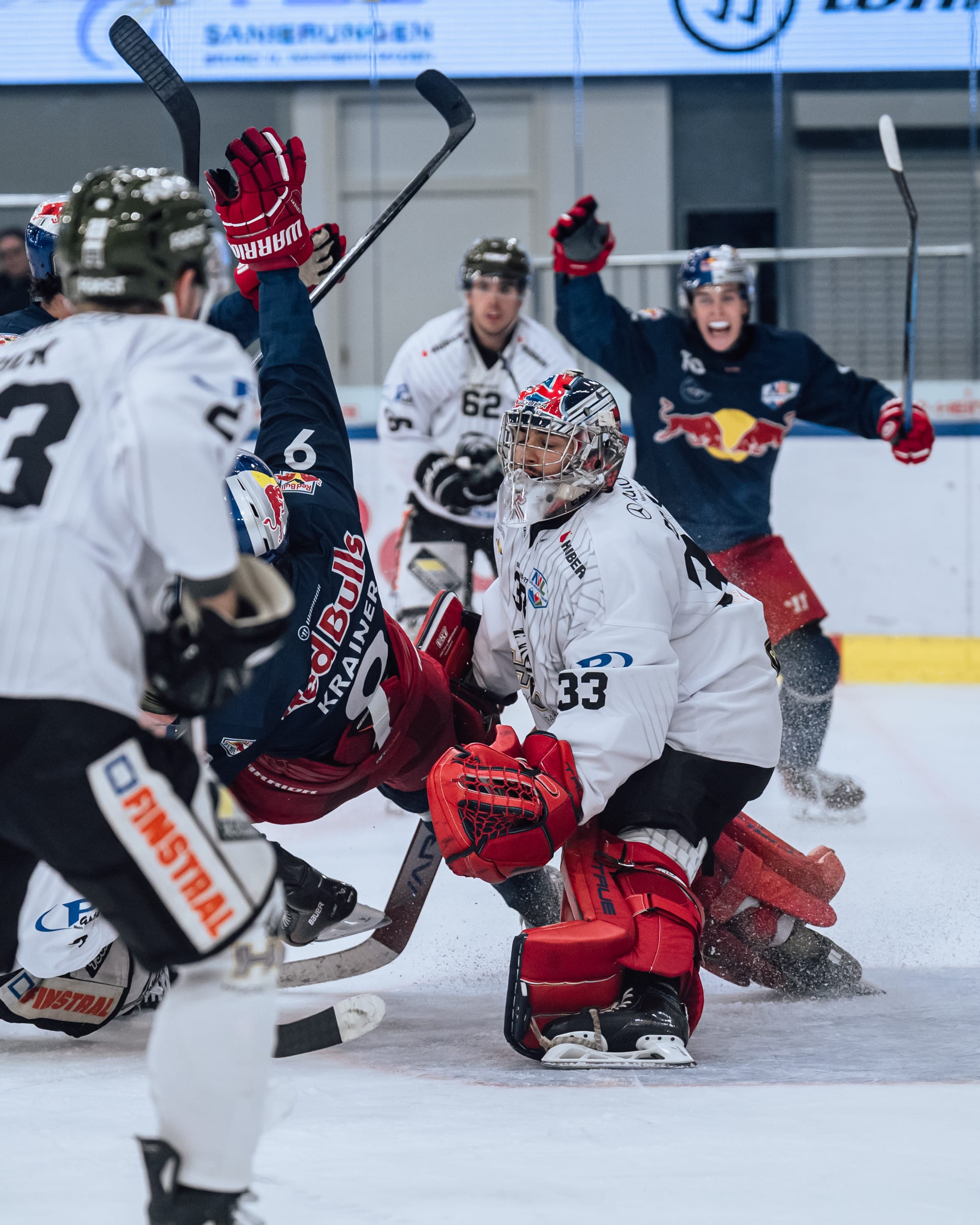 Eishockey-Torhüter mit roten Schützern hält Puck, Spieler jubeln in Salzburg.